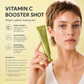 A woman with short light brown hair holds a green tube of Vitamin C Booster Shot against a pale yellow background with product claims and text.